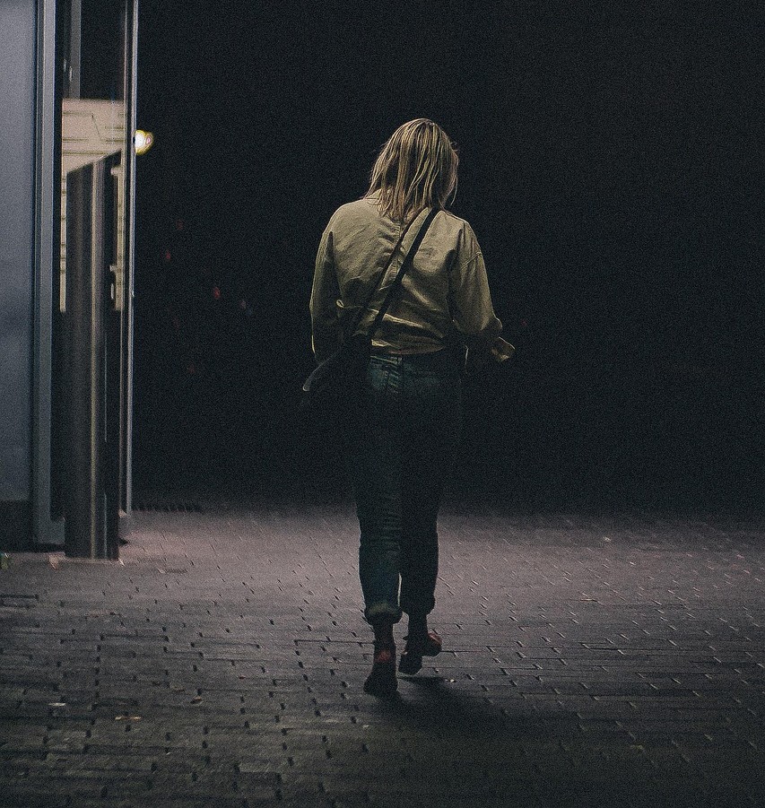 Frau geht alleine nachts auf leerer Straße